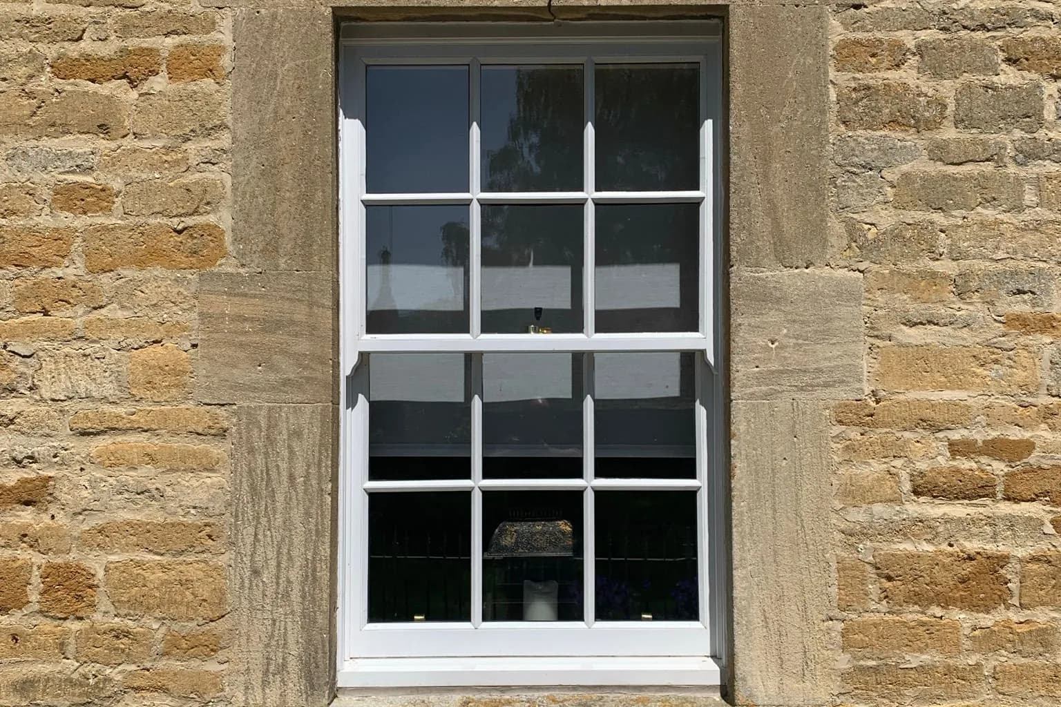 A twelve-pane timber sash window in a dressed limestone surround on a Cotswold stone elevation