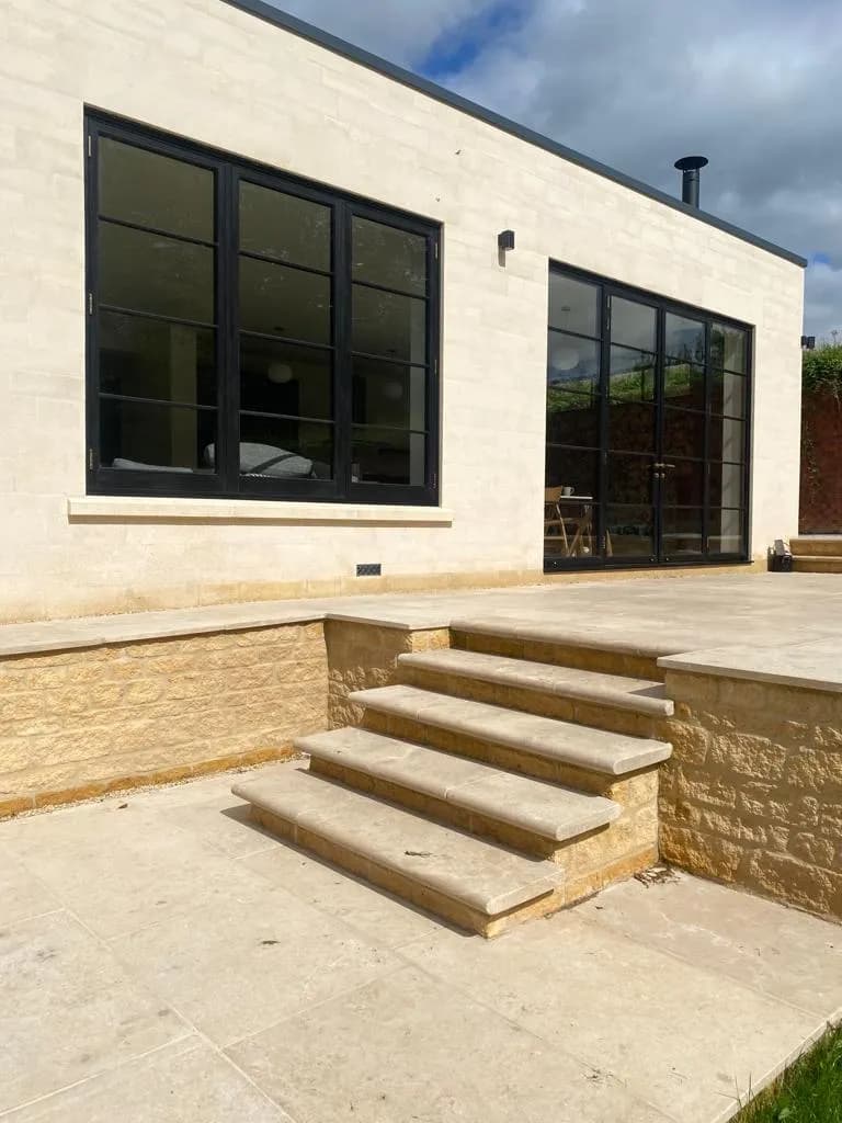 Contemporary stone extension with dark steel-look casement windows and glazed doors opening onto a stone terrace