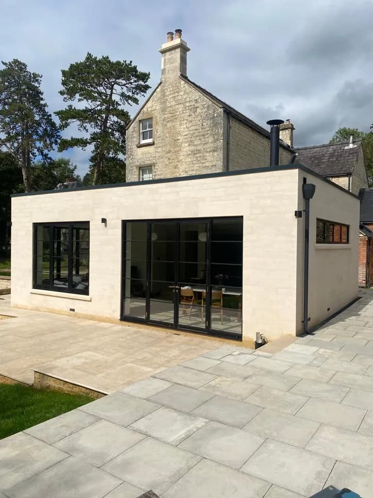 Stone terrace and steps beside the contemporary extension, dark-framed glazing reflecting the garden