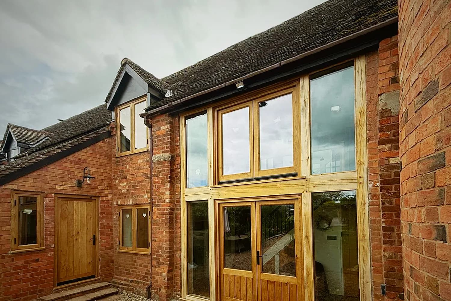 Oak glazing screen filling a brick barn opening, the door set within the frame rather than beside it