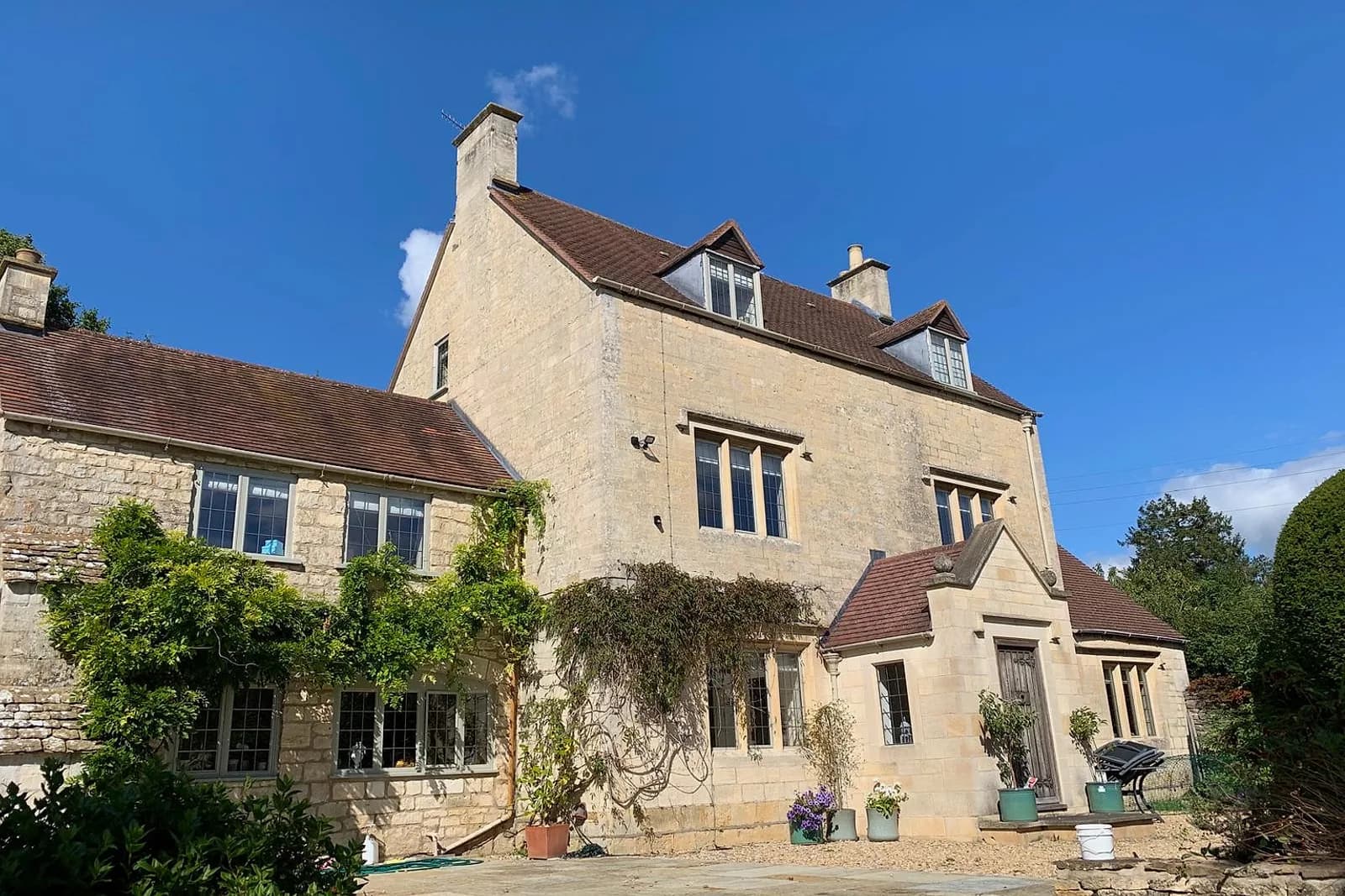Cotswold stone house with painted timber casements and glazed doors along the garden elevation