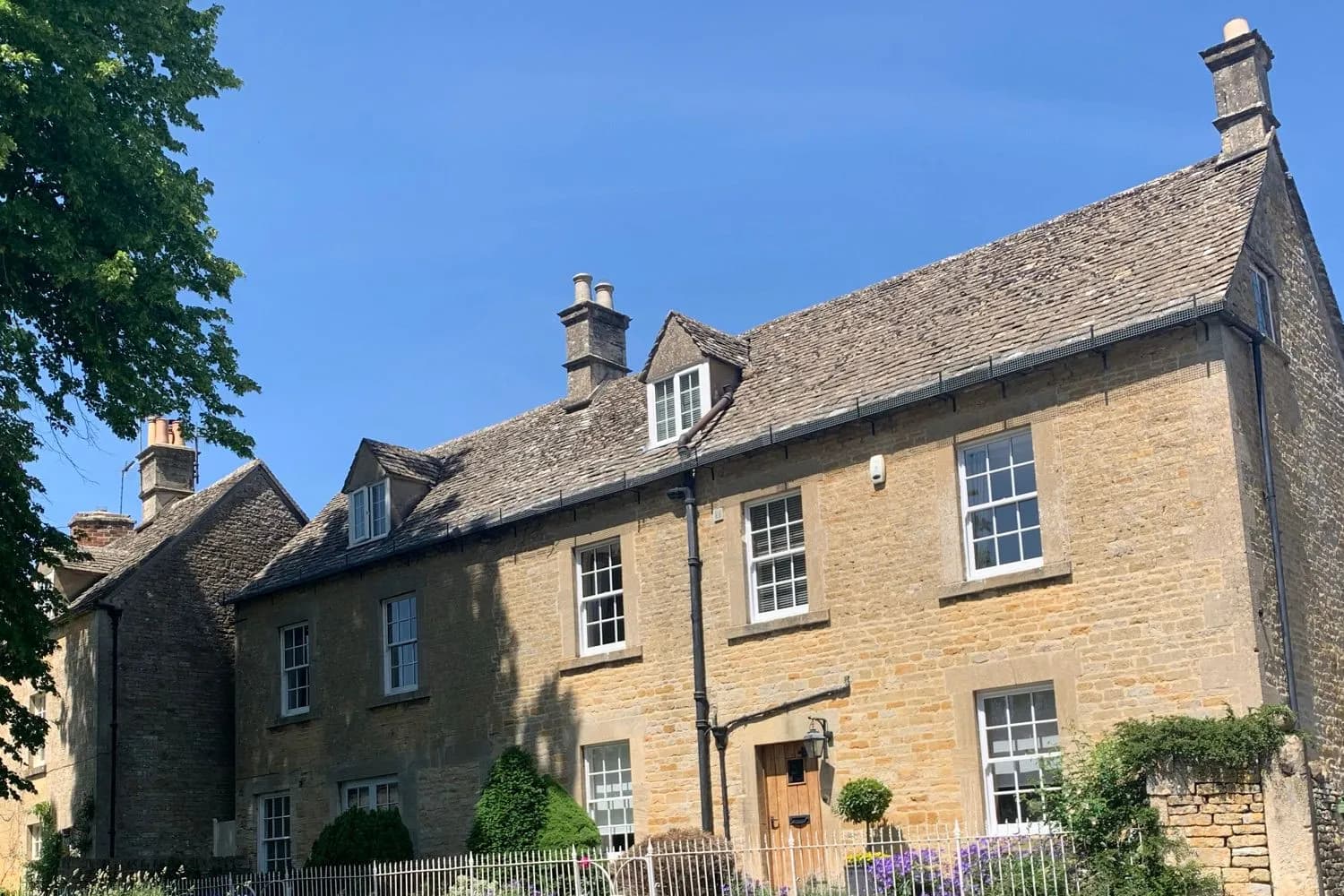 A group of Cotswold stone houses with timber sash windows and stone slate roofs, reading as one continuous village frontage