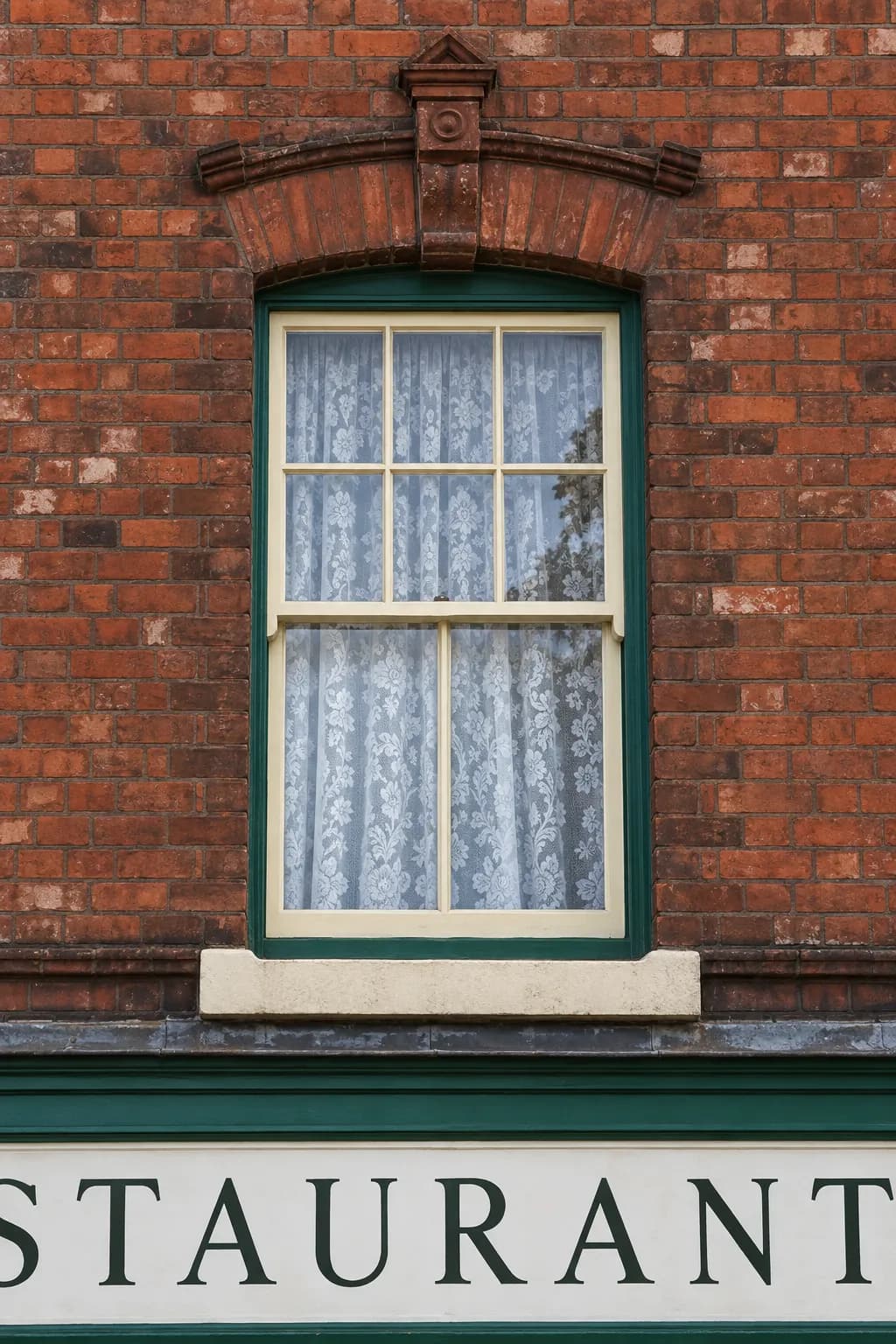 Painted timber sash window with a six-over-two glazing pattern beneath a moulded brick arch, above the Hobbs & Sons restaurant sign