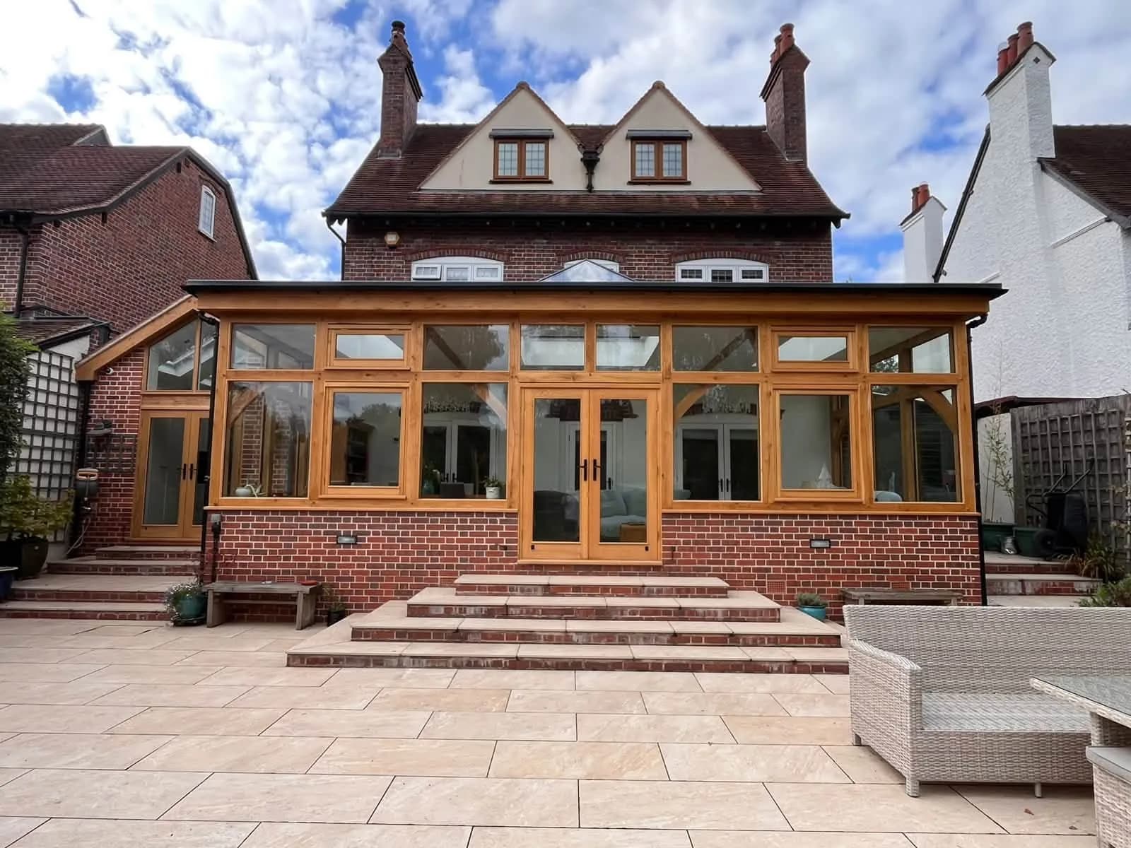 Large oak-framed garden room across the back of a brick house, a run of oak windows and French doors above a brick dwarf wall under a glazed roof