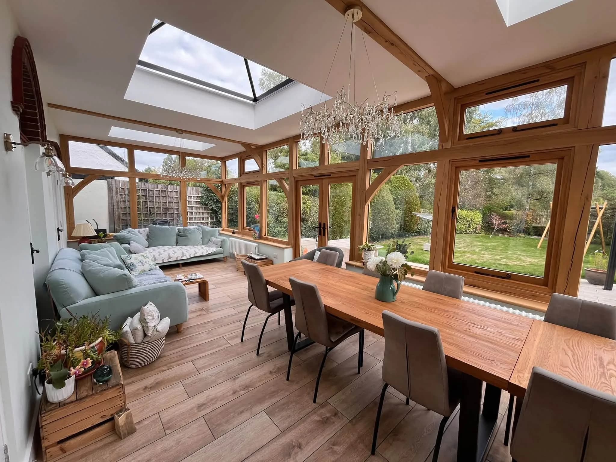 Interior of an oak-framed garden room, exposed posts and braces with oak windows and French doors between them and a glazed lantern above