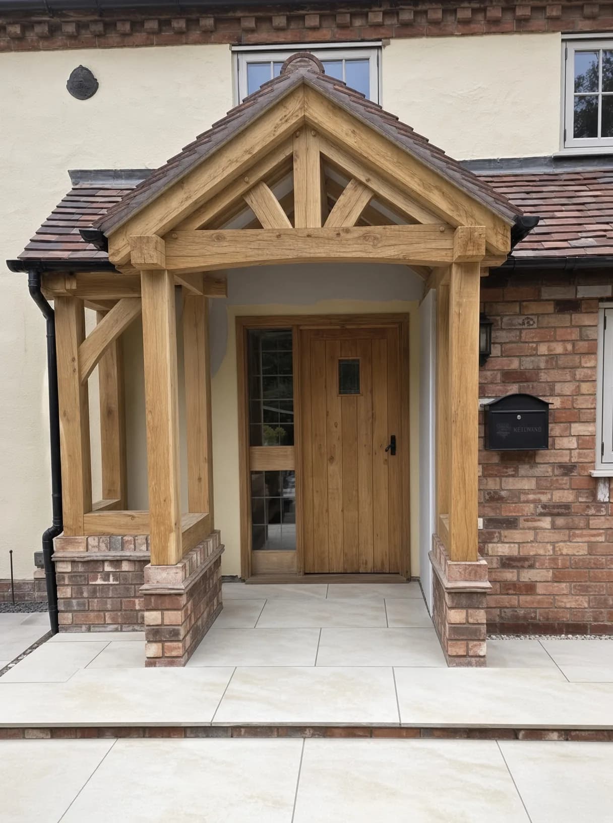 Oak-framed porch with a truss over an oak entrance door, on a rendered house with brick piers