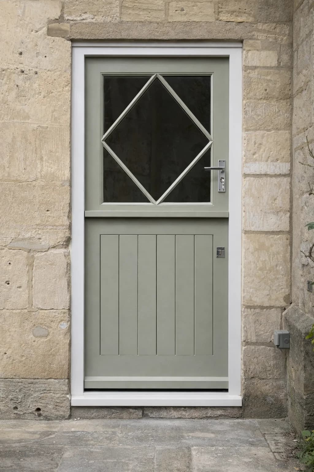 Painted sapele stable door with a diamond glazing pattern to the upper leaf over a boarded lower leaf, in a Cotswold stone opening