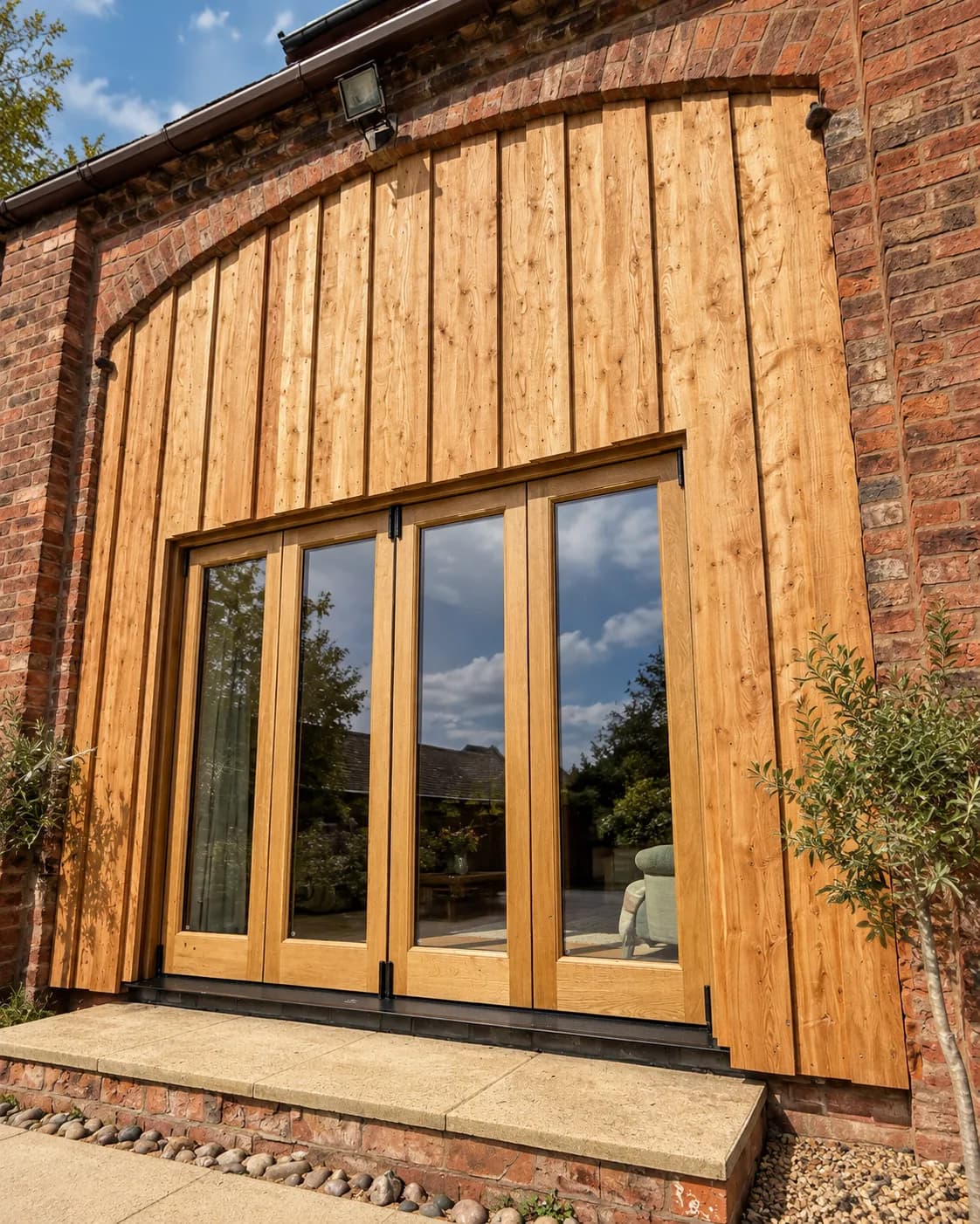 The same brick cart arch with the oak bifolds closed, larch boarding filling the curved head above