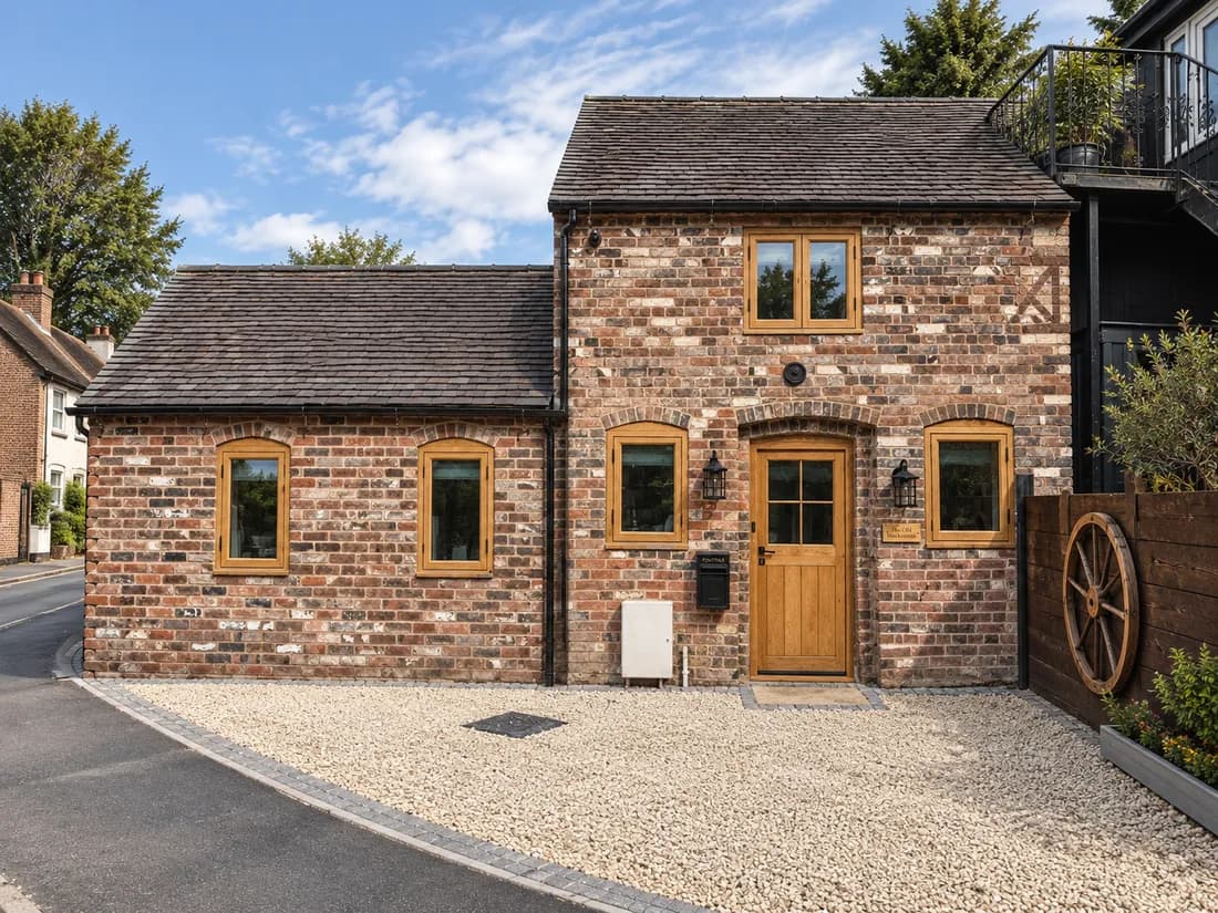 The same building after conversion, with oak windows and an oak front door in the brick openings and a gravel frontage