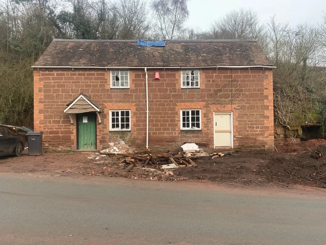 Before: the sandstone cottage with two front doors side by side, painted windows and rubble on the verge as work began