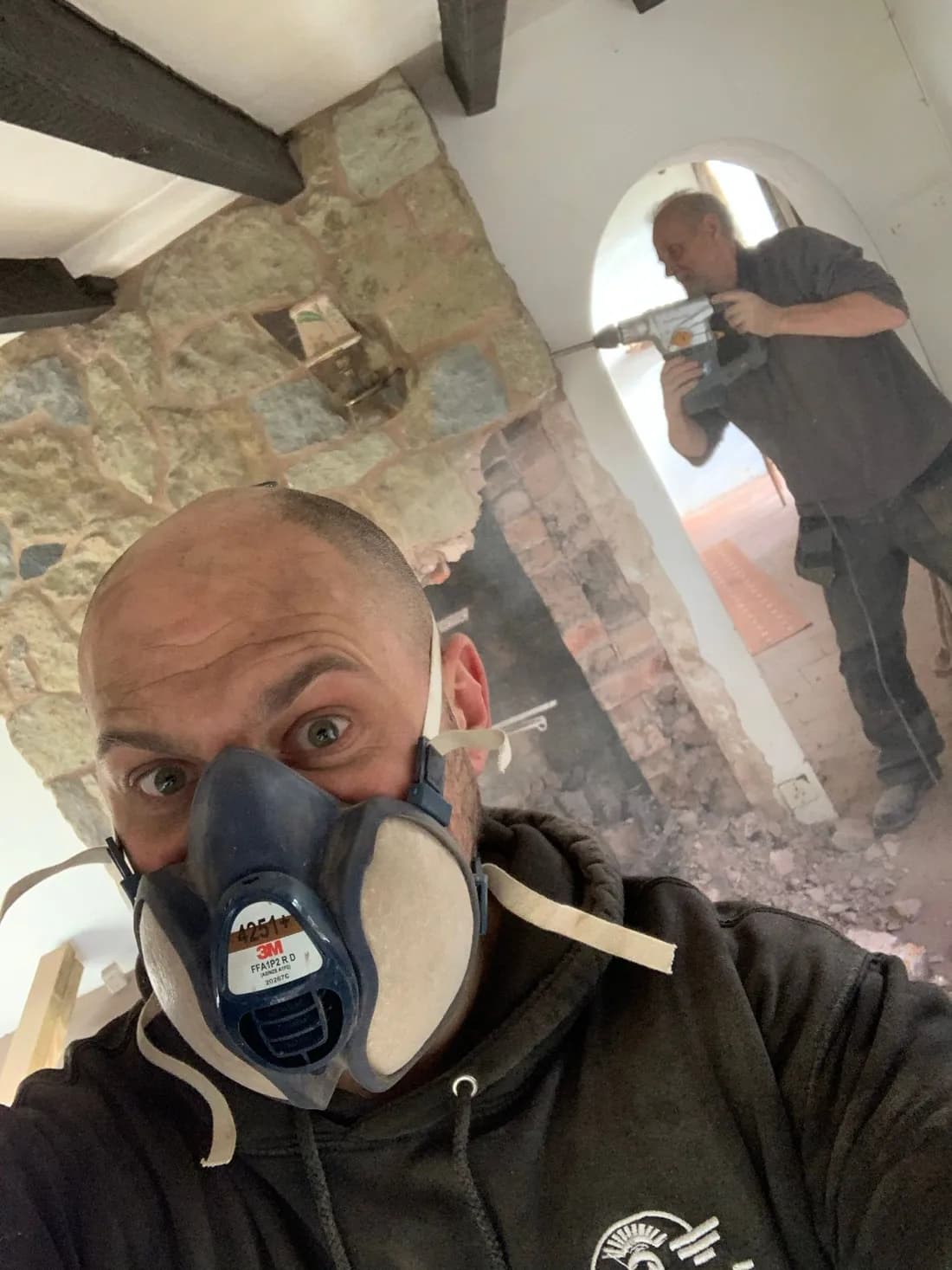 Chris Holland in a dust mask during the strip-out, with a builder working on an arched opening behind him