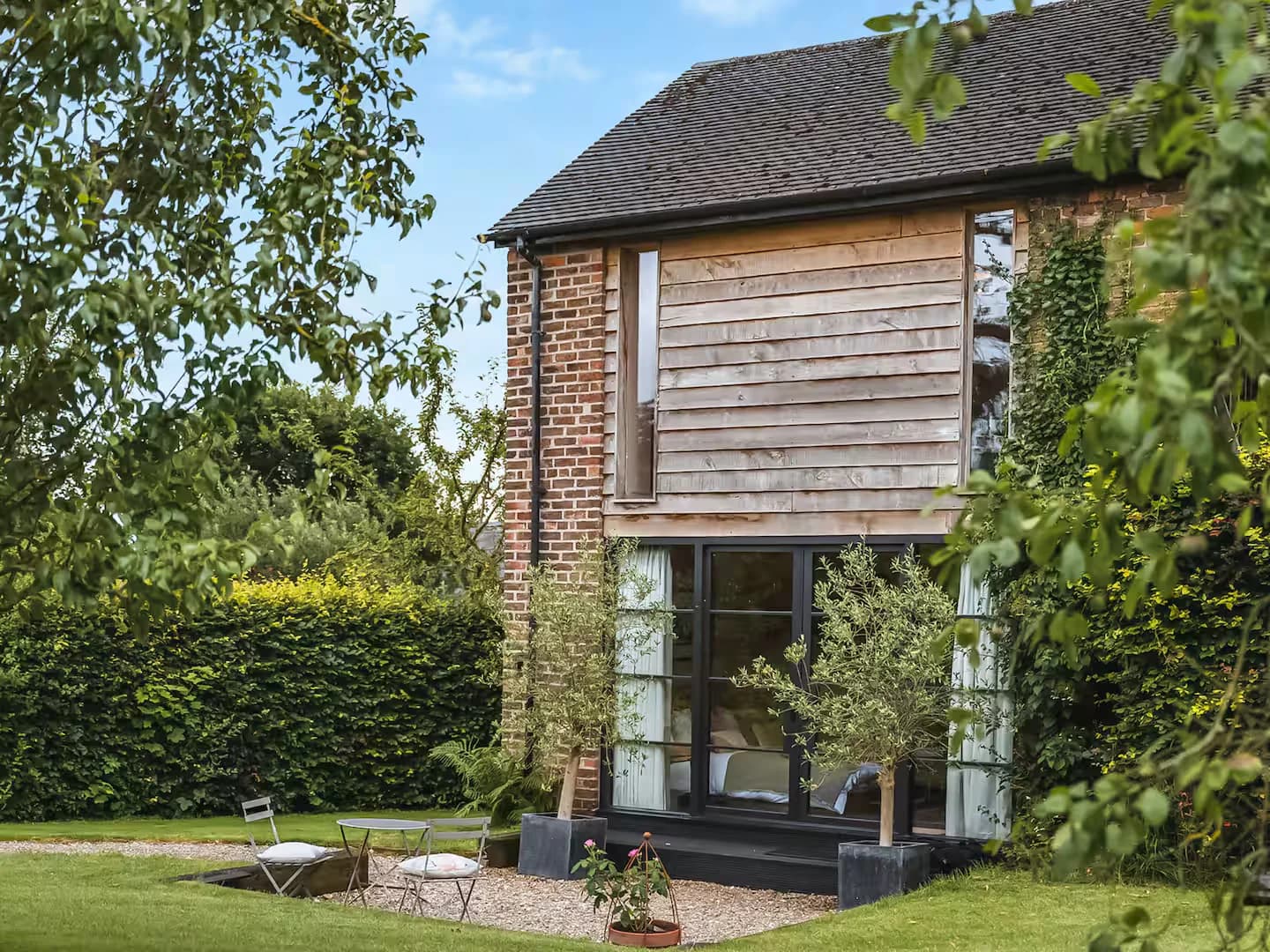 The converted barn from its garden, weatherboarding above brick, steel-look Accoya doors open to the lawn