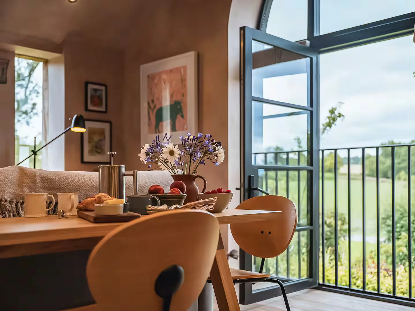 Dining table in the converted barn beside steel-look Accoya doors standing open to a field beyond
