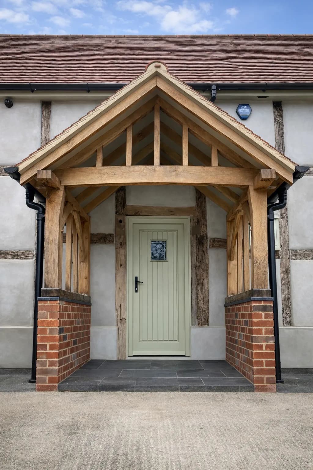 Green oak porch with a pitched canopy sheltering a painted green entrance door, set against a timber-framed elevation