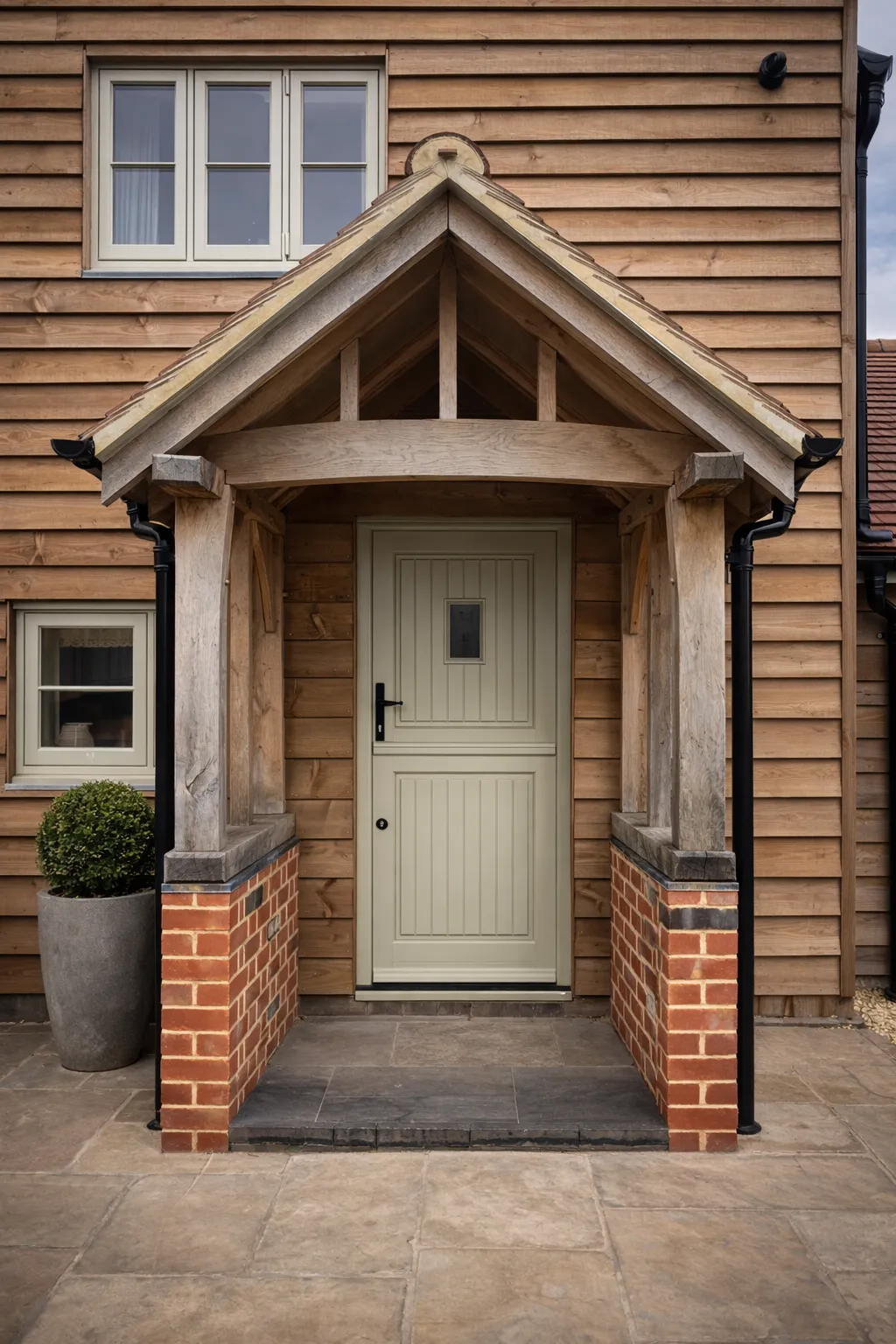 Green oak porch and painted entrance door seen straight on, brick plinth and oak posts
