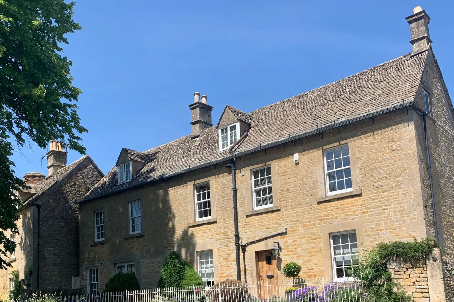 A group of Cotswold stone houses with timber sash windows and stone slate roofs, reading as one continuous village frontage