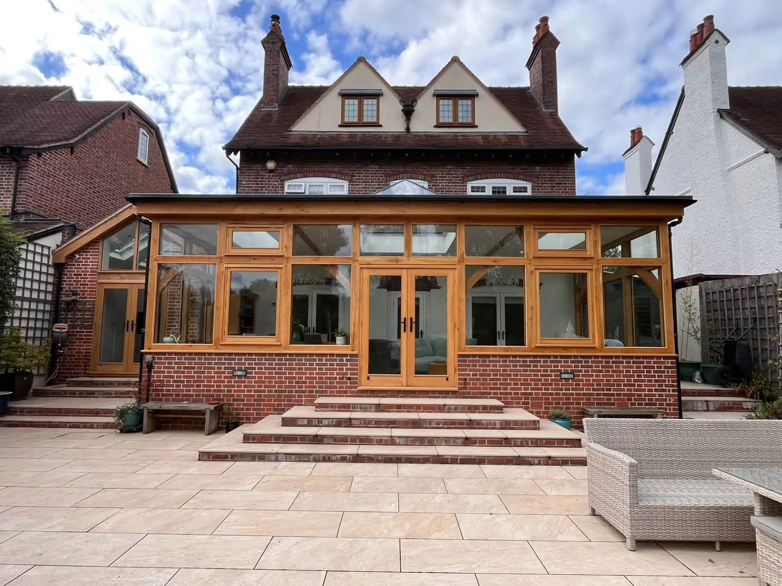 Large oak-framed garden room across the back of a brick house, a run of oak windows and French doors above a brick dwarf wall under a glazed roof